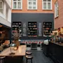 En hyggelig hotellounge med murstensvægge, bogreoler, et langt træbord og en bar. Menuen inkluderer BUBBEL, VITT VIN, ROTT VIN, ROSE, CIDER. Nyd og skål!