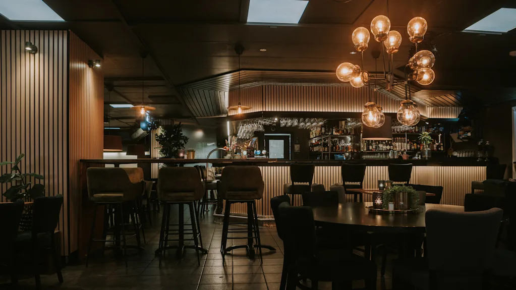 En dunkelt oplyst bar med stole, borde og pendellamper; ingen kunder, rolig atmosfære.