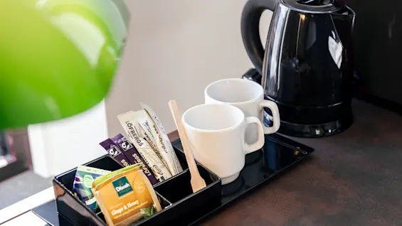 A tea and coffee station at Quality Hotel The Book, with a kettle, mugs, and various sachets of tea and sugar, including Ginger & Honey.