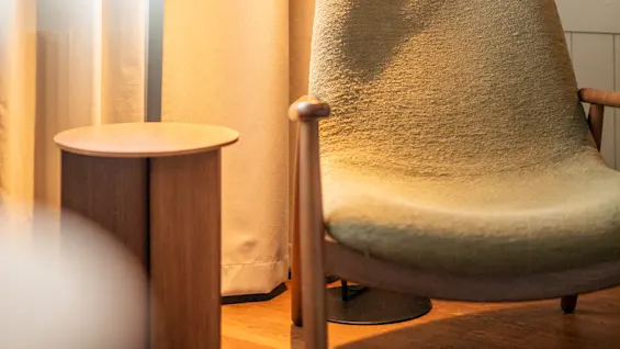 Fåtöljen vilar i ett mysigt hörn upplyst av en golvlampa; texturtapet med blommönster och tunga gardiner förstärker den varma atmosfären.
