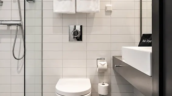 Modern hotel bathroom featuring white wall tiles, dark flooring, a shower, toilet, and sink.