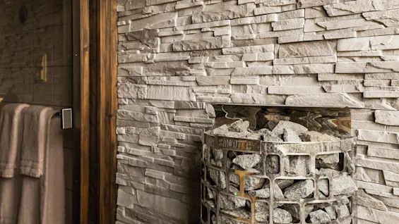 Saunan kiuas kivineen kiviseinän vieressä, pyyhkeet näkyvissä lasioven läpi Comfort Hotel Linköping Cityssä.