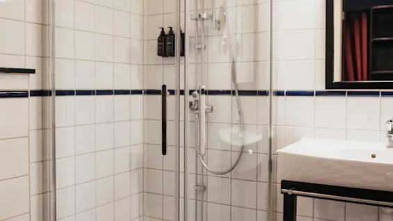 A clean and modern bathroom with a shower, toilet, and sink, featuring a blue and white checkered floor. Home Hotel Kung Oscar.