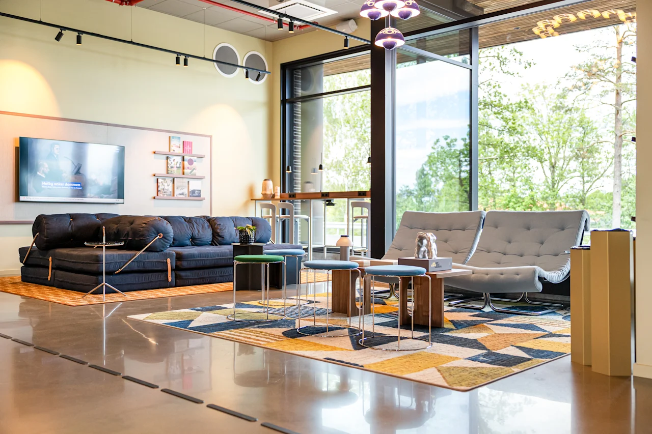 A modern and inviting lounge area with comfortable seating, a large TV, and big windows overlooking lush greenery.