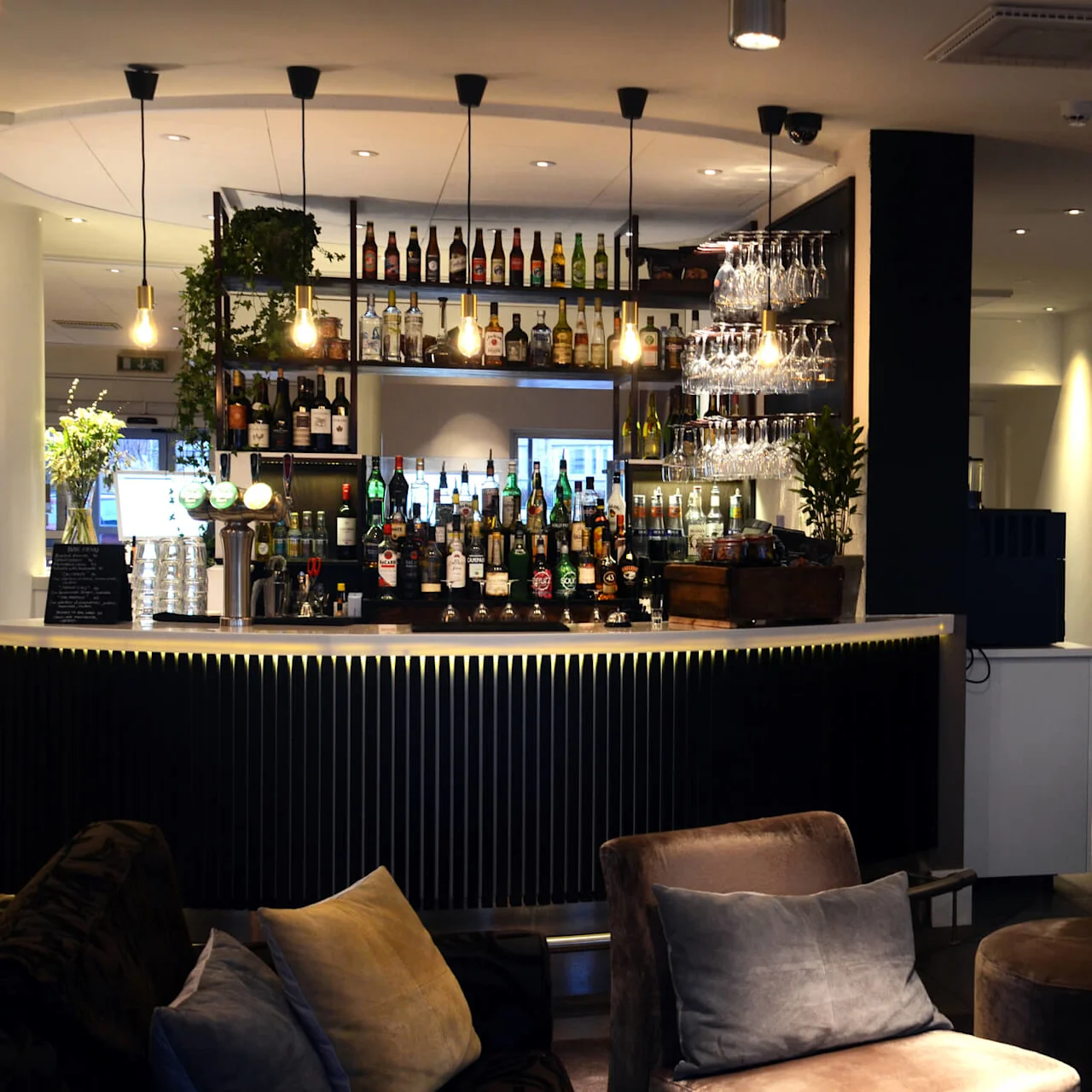 A well-stocked bar with various bottles, softly lit, surrounded by comfortable seating area in an upscale, modern ambiance.