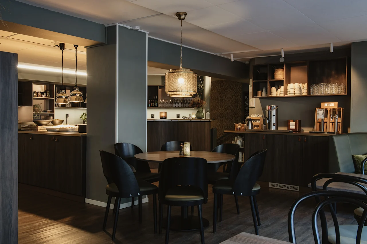 En mysig matplats med ett runt bord och stolar, en självbetjäningsstation med kaffe och juice samt en serveringsdisk.