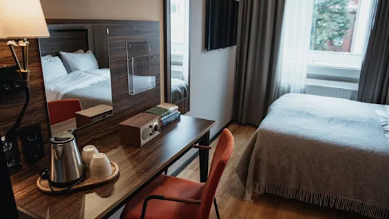 Moderni hotellihuone, jossa on mukava sänky, toimiva työpiste kuumien juomien tarjoilupisteellä ja ikkunanäkymä.