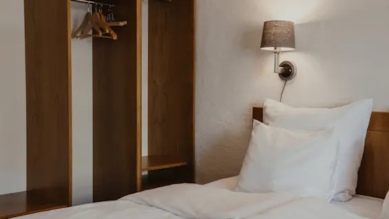 Viihtyisä hotellihuone, jossa on sänky, seinävalaisin ja avoin puinen vaatekaappi.