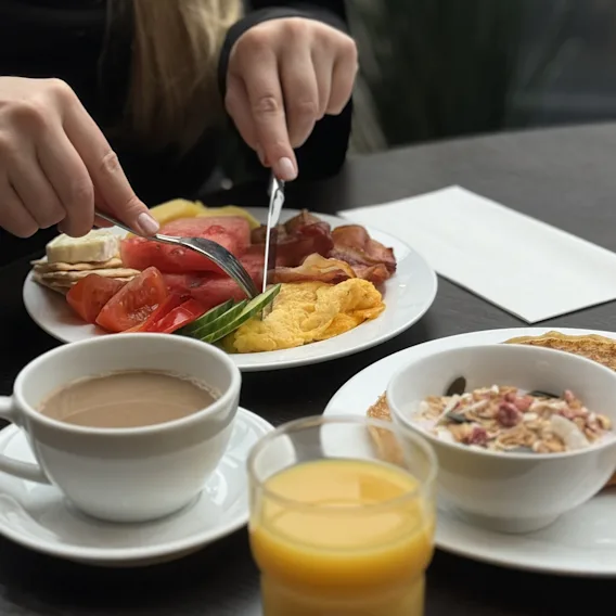 Frokosttallerken med eggerøre, bacon, frisk frukt, kaffe, appelsinjuice og granola på et bord.