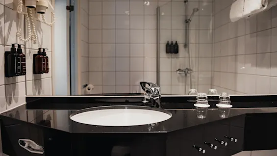 Ett rent och modernt hotellbadrum med handfat, spegel och dusch, med viktiga bekvämligheter lättillgängliga.
