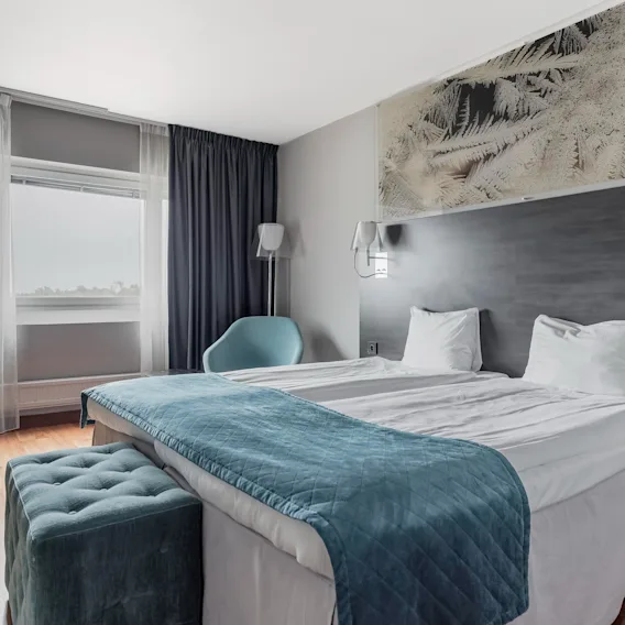 Ett modernt dubbelrum på hotell med en stor säng, blått överkast och ett fönster.