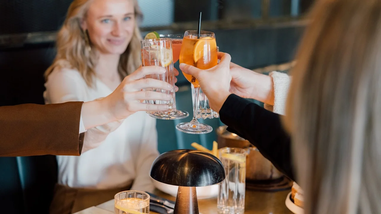 Glasses with drinks being clinked, held by people seated at a dining table, celebrating in a warmly lit restaurant.