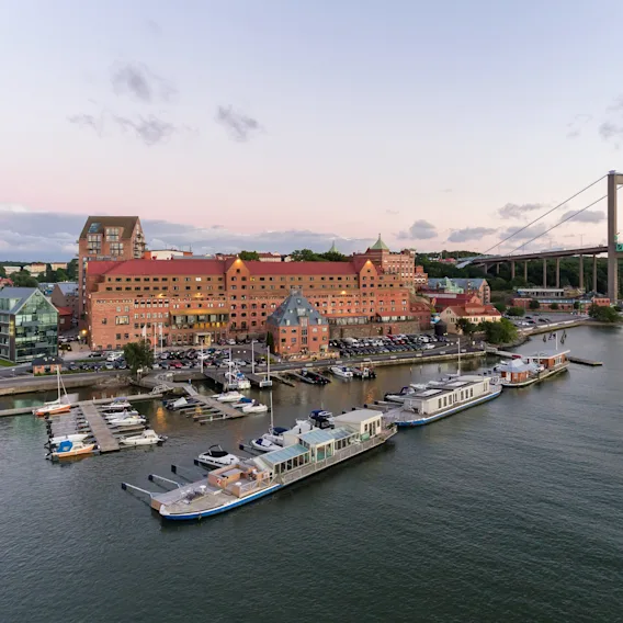 Flygfoto över ett hotell vid vattnet i Göteborg med en bro i bakgrunden under en rosa himmel.