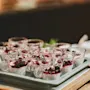 Small glass cups hold chia pudding topped with dark berry sauce, arranged neatly on a tray, all placed on a wooden table in an indoor setting.