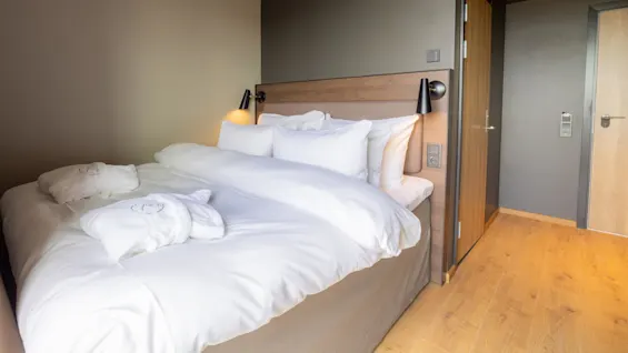 En snyggt bäddad säng med vita lakan i ett städat hotellrum. Det finns inga textelement.