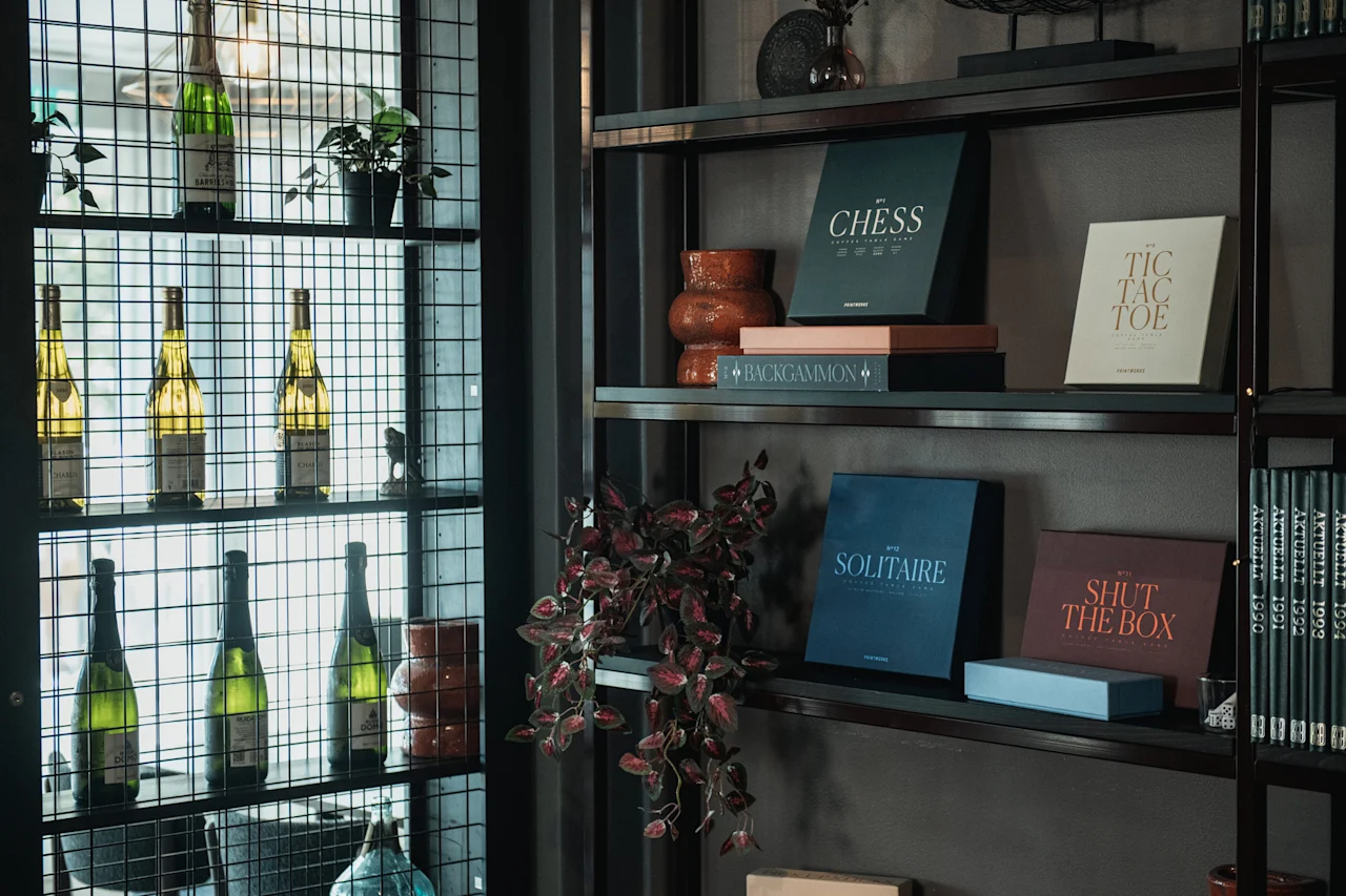 En stilfull hylla med flaskor och växter, tillsammans med brädspel som Schack, Tre i rad, Backgammon, Solitaire och Shut the Box.