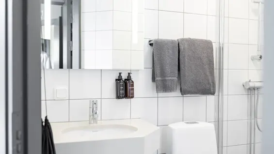 Valoisa ja puhdas moderni kylpyhuone, jossa on valkoiset laatat, pesuallas, wc ja suihkutila tuoreilla pyyhkeillä.