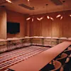 Et moderne konferanserom med et U-formet bord, stoler, en stor skjerm og unik belysning, klart for et møte.