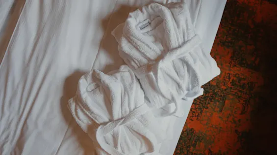 To myke hvite badekåper pent brettet på en seng, klare for et avslappende opphold.