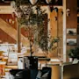 En hyggelig lounge har en mørk sofa med stribede puder, omgivet af løvrige planter og varme trævægge. Elegante pendellamper hænger fra loftet og oplyser rummet.