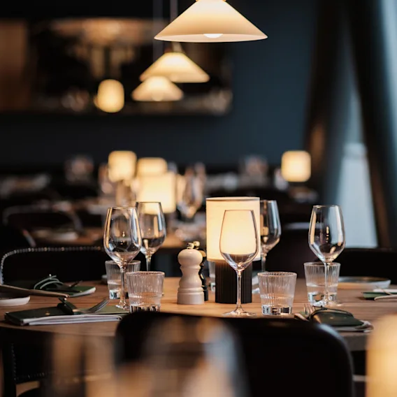 Dining table set with wine glasses and plates, surrounded by softly lit lamps in a dimly lit restaurant.