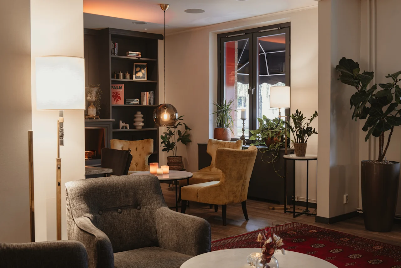 A cozy hotel lounge with comfortable armchairs, warm lighting, and lush plants, inviting relaxation. PALM. Home Hotel Kung Oscar.