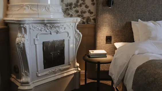 Ett mysigt hotellrum med en dekorativ vit öppen spis, en bekväm säng och ett sängbord med böcker.