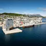 Quality Hotel Harstad, en moderne bygning på en brygge i en livlig byhavn med et stort skip fortøyd, omgitt av åser og fjell.