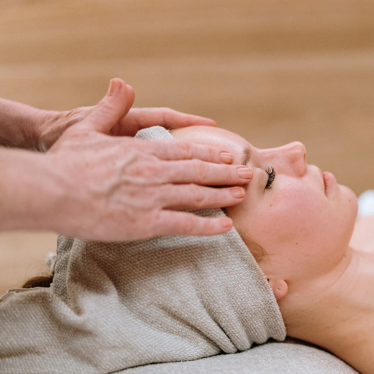 En person modtager pandemassage mod en neutral baggrund, ligger ned med lukkede øjne, dækket af et håndklæde.