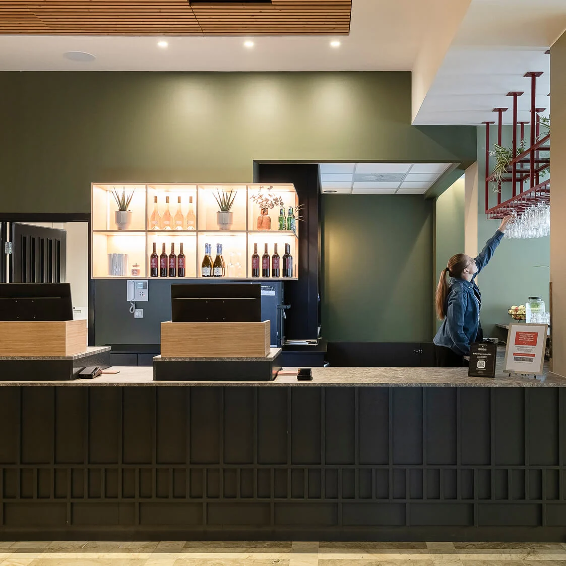 En kvinna står vid en incheckningsdisk på hotell och når efter en hyllad display i en modern lobby.