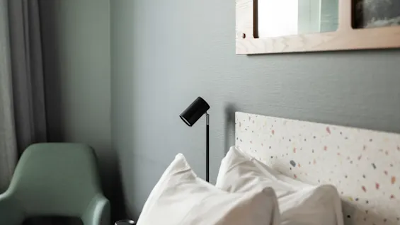 A modern and inviting bedroom with a comfortable bed, soft pillows, a sleek black lamp, and a stylish green chair.