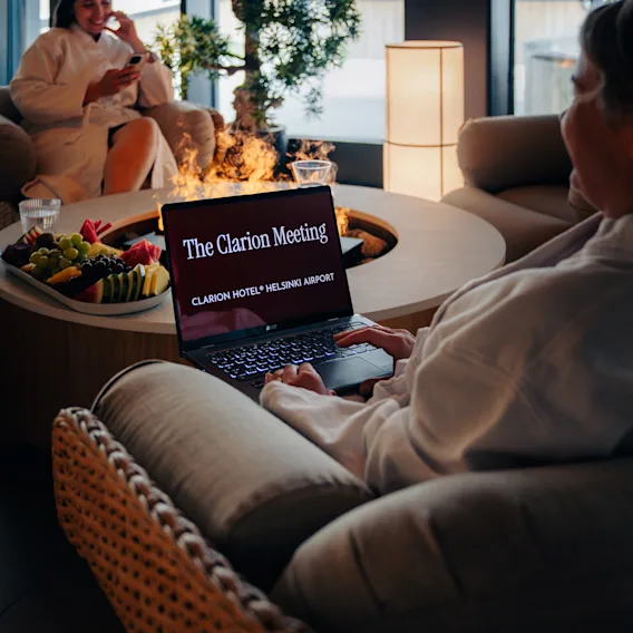 Kylpyläkokous Clarion Hotel Helsinki Airportissa. Ihmisiä kylpytakeissa, yksi kannettavalla tietokoneella näyttäen 'The Meeting HOTEL HELSINKI AIRPORT'.