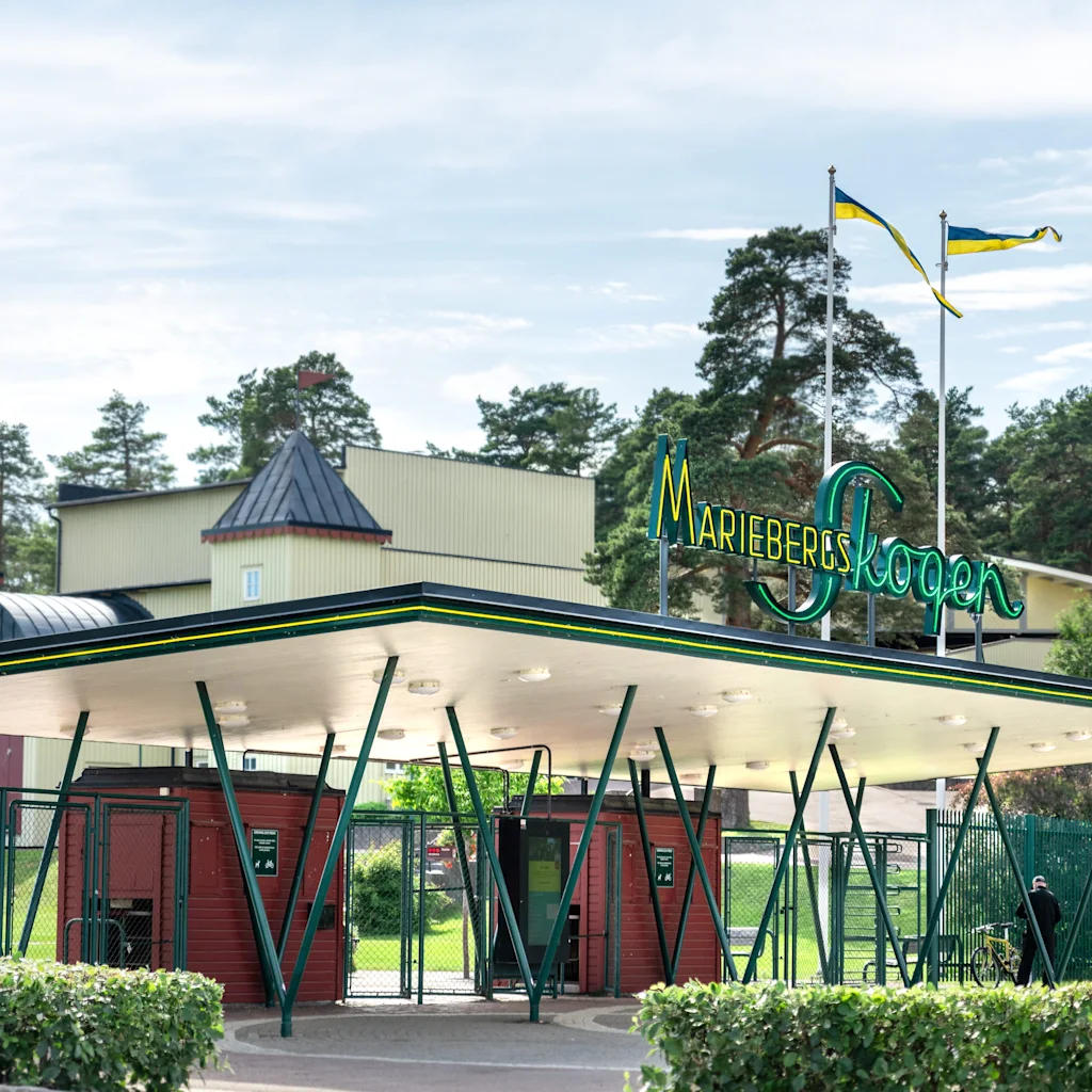 Entrance to Mariebergsskogen in Karlstad, a park with a large canopy and ticket booths, surrounded by trees.