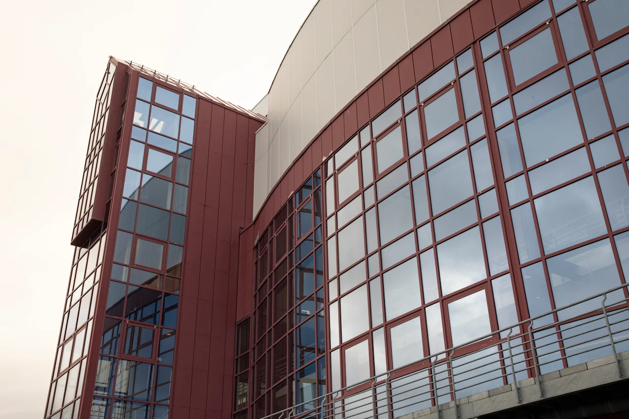 Moderni rakennus, jossa on punaruskea julkisivu ja lukuisia heijastavia ikkunoita, kaarevalla muotoilulla ja ulkokäytävällä.