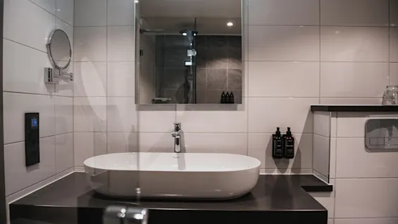 Et godt opplyst, moderne bad med en elegant hvit vask, et stort speil og mørk benkeplate, klart for personlig pleie.