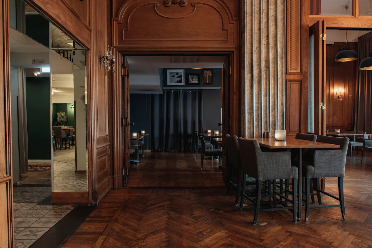 En mysig hotellounge med träväggar, fiskbensparkett och bord med stolar, redo för gäster. Home Hotel Grand, Helsingborg.