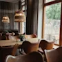 A cozy restaurant interior with warm lighting, wooden tables, and leather chairs, looking out onto an outdoor patio.