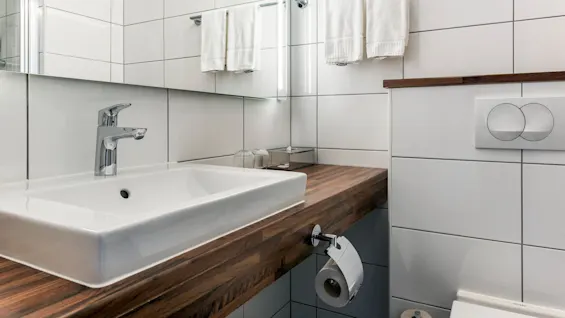 Et moderne baderomsvask og kran på en benkeplate av tre, med flislagte vegger og håndklær hengende ovenfor.