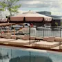 Et bassengområde med solsenger og parasoller med utsikt over en marina med båter, som antyder en avslappende utendørs setting.