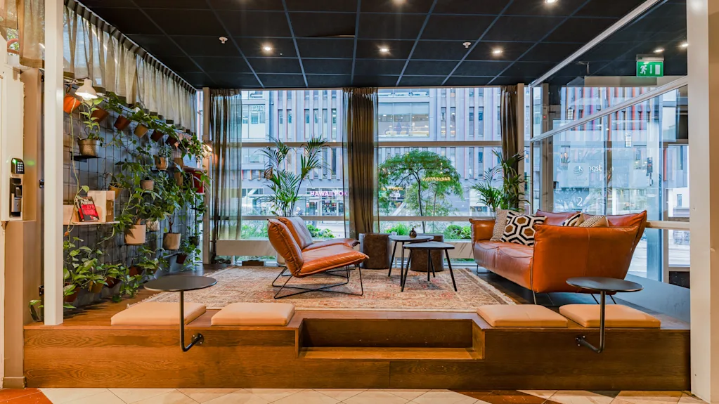 A modern and cozy hotel lobby lounge with leather seating, green plants, and large windows.