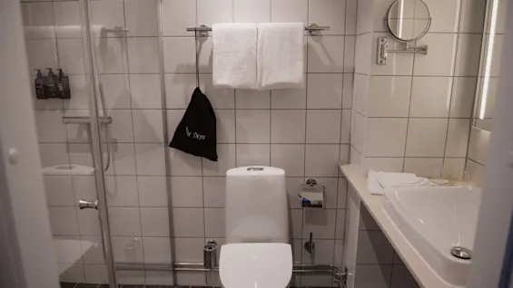 Ett rent och modernt hotellbadrum med dusch, toalett, handfat och en väska märkt Hair Dryer.