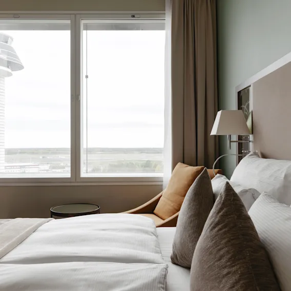 Ett inbjudande hotellrum med en bekväm säng och ett stort fönster med utsikt över ett modernt torn och det avlägsna landskapet.