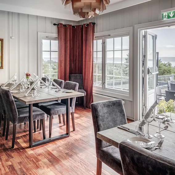Elegant spisestue med dekkede bord og åpne dører som leder til en terrasse med vakker havutsikt.