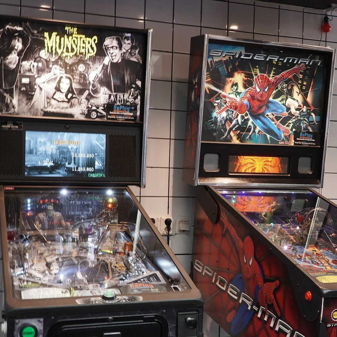 Pinball machines with "The Munsters" and "Spider-Man" themes in an indoor recreational space.