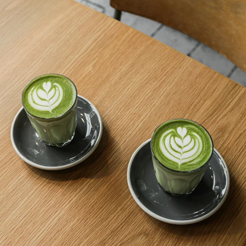 To livlige grønne lattes med delikat latteart står på et varmt træbord og inviterer til et øjebliks ro.