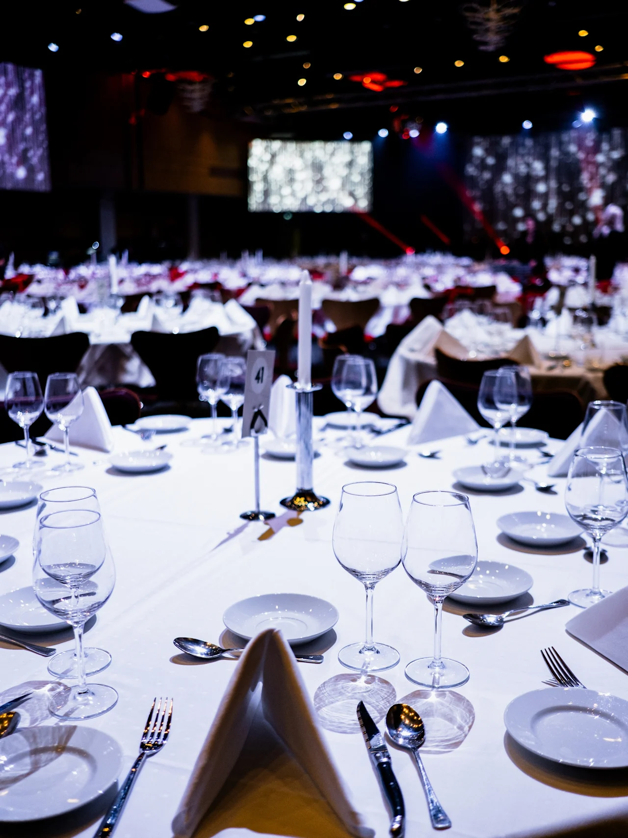 Elegant spisebord dekket med flere glass, tallerkener og bestikk, under dempet belysning i en formell eventlokale. Et skilt merket "4" står på bordet.