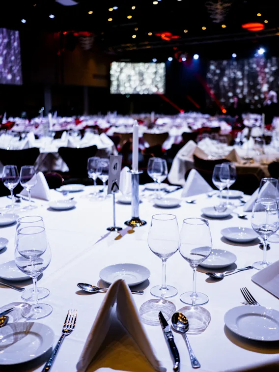 Elegant spisebord dekket med flere glass, tallerkener og bestikk, under dempet belysning i en formell eventlokale. Et skilt merket "4" står på bordet.