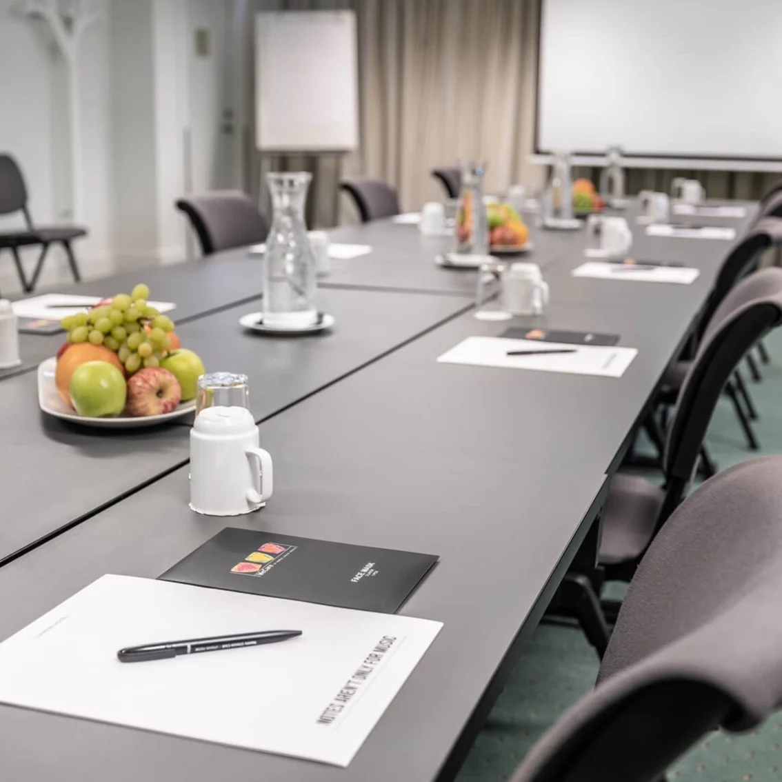 A conference room with a long table, papers, and a projector screen in a business setting.