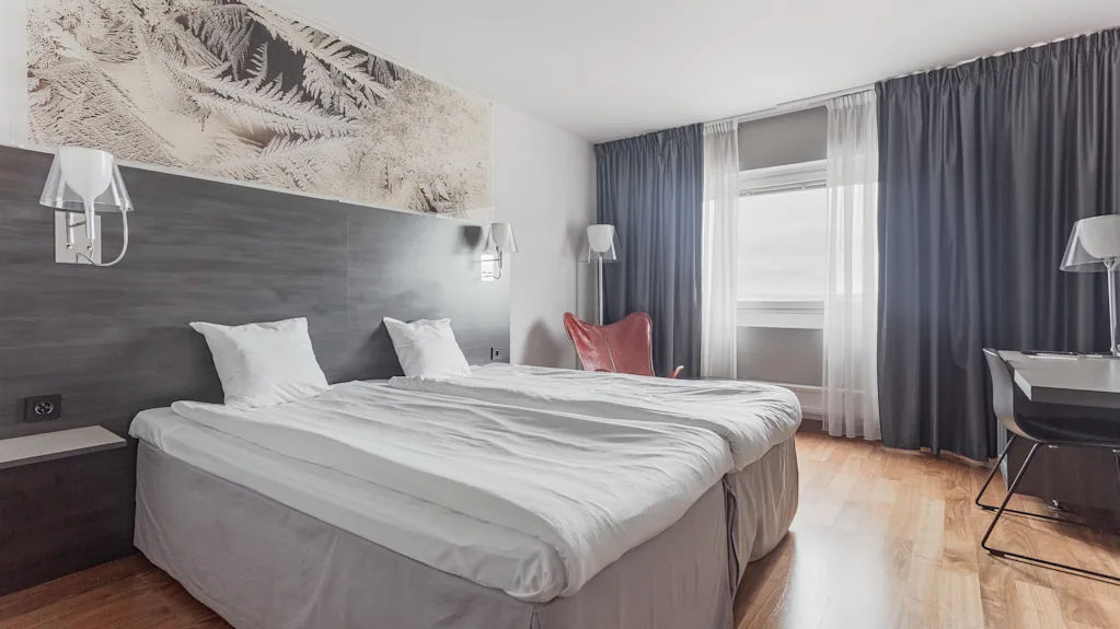 A welcoming hotel room with twin beds, a workspace, and a large window providing natural light.