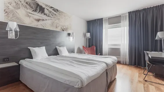 A welcoming hotel room with twin beds, a workspace, and a large window providing natural light.
